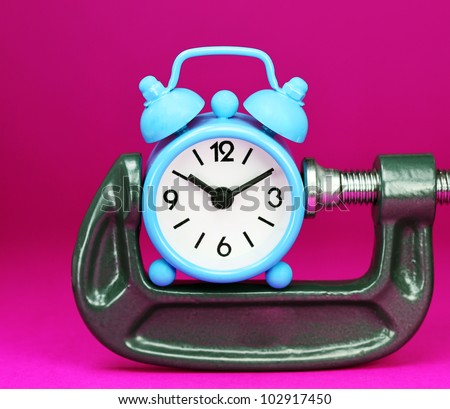 A pastel blue colored  alarm clock placed in a Grey clamp against a pastel purple background, asking the question do you manage your time effectively.