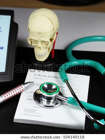 A doctorÃ¢Â?Â?s desk showing a green stethoscope and pen, resting on a sick certificate pad, with the other doctors tools of the trade on desk including a blood pressure machine and model of a human skull.
