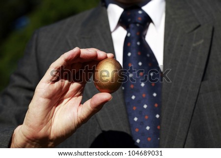 A well dressed businessman holding a golden nest egg in front of his immaculate suit.