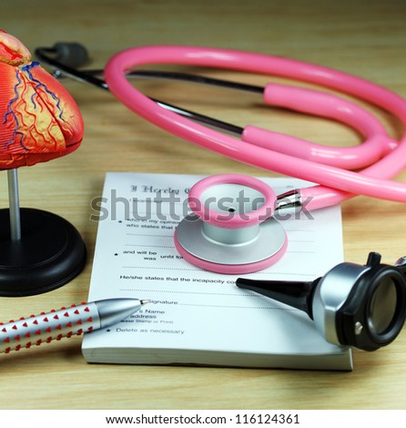 A doctorÃ¢Â?Â?s desk showing a pink stethoscope, resting on a sick certificate pad and a detailed model of the human heart in the background, and in the foreground the doctorÃ¢Â?Â?s pen.