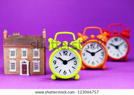 Four colored alarm clocks next to your next house asking the question is it time to up size before the housing boom takes off!