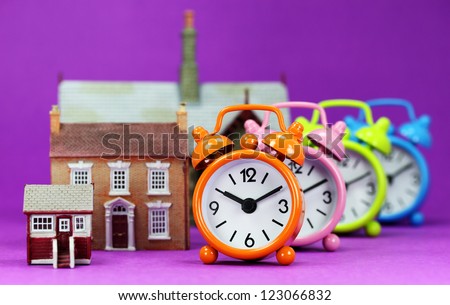 Four colored alarm clocks next to three houses ranging from small, medium and large homes, asking the question is it time to wake up to the housing market!