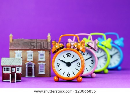 Four colored alarm clocks next to two houses a small and medium houses asking the question is it time to wake up to the housing market!