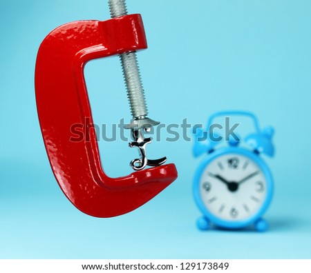 A silver pound symbol placed in a red clamp with a pastel blue background, with a blue alarm clock in the background  indicating the pressure on the pound sterling.