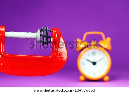 A silver Dollar symbol placed in a red clamp with a purple background, with an orange alarm clock in the background indicating the pressure on dollar.