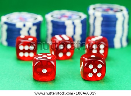 Five red dice with white numbers, with some gambling chips in the background set against a green background.