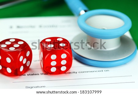 Two dice placed on a a doctors medical certificate pad next to his light blue stethoscope, asking the question do you gamble with your health care?