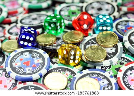 Five translucent colored dice laying on a pile of gambling chips of various denominations, with some gold coins also lying on the gambling chips