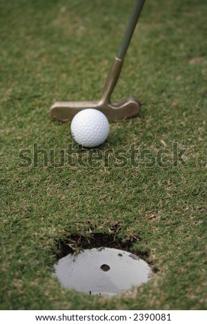 Golfer about to make a putt, showing golf ball, putter and hole