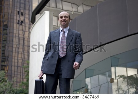 Businessman walking through the city with briefcase and office skyline behind him
