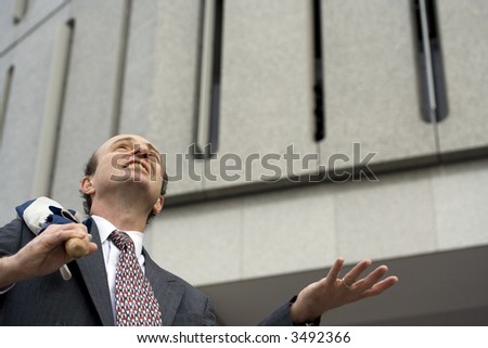Businessman with umbrella over his shoulder walking down the steps and holding his hand in the air to feel the rain coming down on his way to his next appointment with the tall building behind him