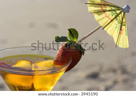 Beautifully made yellow cocktail with a strawberry and cocktail umbrella with the beach in the background