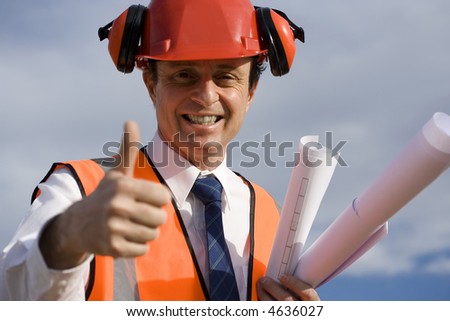 Engineer looking happy, with a beautiful blue sky behind him, wearing a red safety helmet, wearing an orange high visibility vest and carrying the blueprints afar being successful