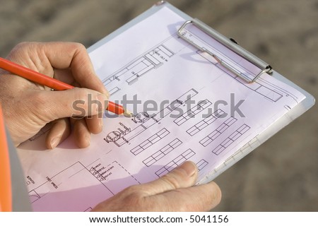 Engineer making changes to the blueprints on a clipboard with a pencil