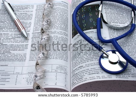 Doctor’s medical dictionary open at the chromosome page with a tape measure laid out like DNA also with a doctors blue stethoscope and pen laying on the open dictionary