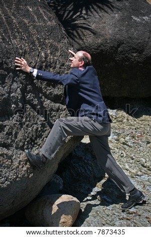 Businessman wearing business attire at the base of a cliff trying to reach the top representing a business challenge