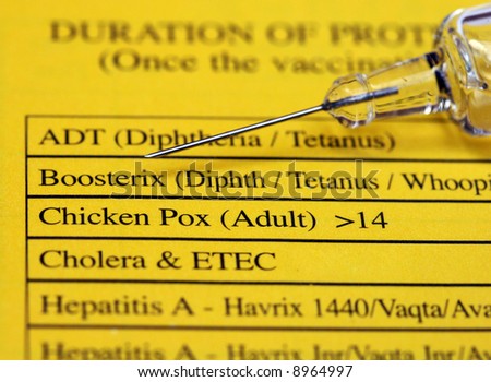 A syringe containing a vaccine lying on the back of a patient’s vaccination yellow record book, also showing the list of vaccinations required