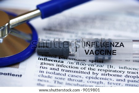 A syringe containing the influenza vaccine laid on a doctors medical dictionary open at the influenza page.