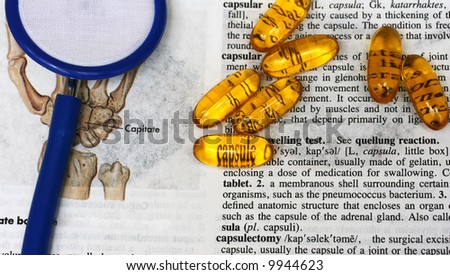 Capsules laying on a medical dictionary with the word capsule seen through the yellow capsule.