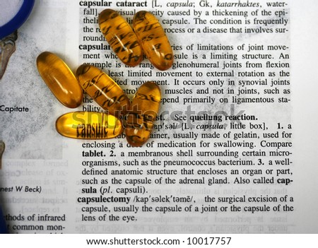 Capsules laid on a medical dictionary with the word capsule seen through the yellow capsule.