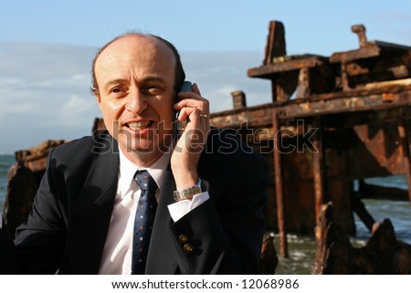 Businessman explaining on his mobile telephone that the shipwreck cannot be salvaged, as it had run aground years ago,