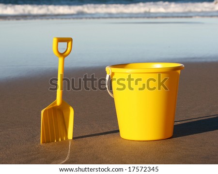 A yellow plastic bucket and spade on the beach, with the tide behind coming in.