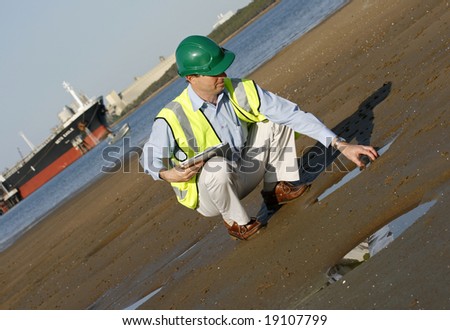 An environmental engineer, wearing protective clothing about to take a water sample, from the mudflats in the estuary.