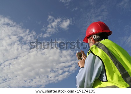 An environmental engineer examining a sample showing the beautiful blue sky, wearing an yellow reflective vest and red safety helmet.