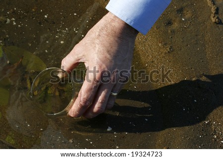 An environmental engineer, in the mangroves taking a water sample, with a glass beaker, also showing engineers hand