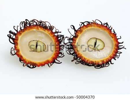 A close up of a rambutan fruit cut in two revealing the succulent white flesh protected by red hairy shell.