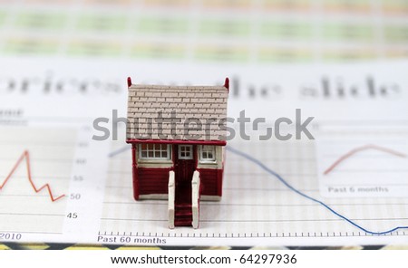 A toy house placed on a graph where the red trend line is heading south, indicating that the owners of this property are facing tough financial times ahead.