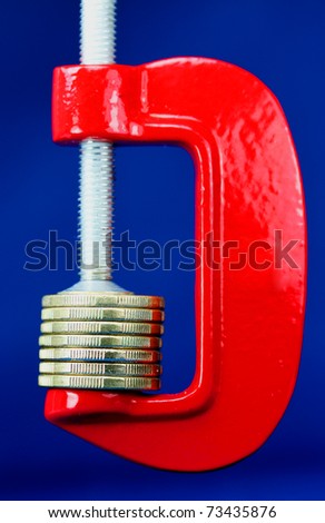 A stack of gold coins in a red clamp with a dark blue background, indicating the pressure is on to make ends meet.