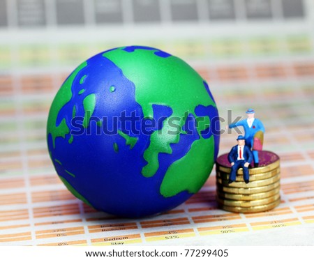 Two businessman one sat and one stood on a pile of golden coins next to a globe of the world, with Europe prominent.