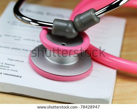 A female doctors desk showing a pink stethoscope, pen and sick certificate pad.