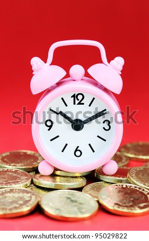 A pink alarm clock placed on some golden coins with a red background, asking the question how long before your investment matures?