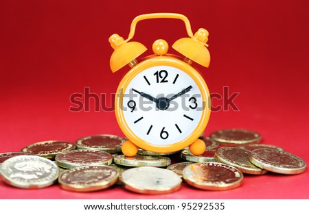 An Orange alarm clock placed on some golden coins with a bright red background, asking the question how long before your investment matures?