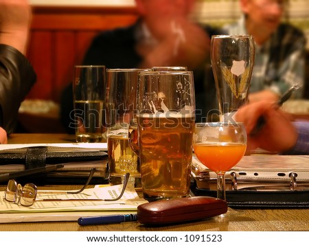 half empty beer glasses on table and blurred faces and men\'s hands around and in the background