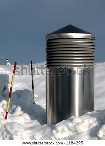 metal chromed air shaft above the ground in snow and tiny, tiny church tower in background