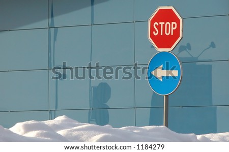 stop sign and keep left traffic sign in snow in front of a glass wall