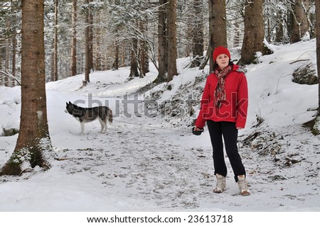young woman dressed in red in a snowy forest, in the background a siberian husky dog on the leash