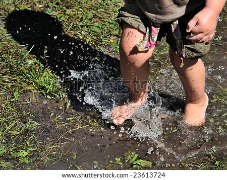 a small girl stomping through a muddy water puddle