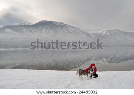 woman dressed in red hugging a siberian husky dog on the shore of an alpine lake in winter on snow