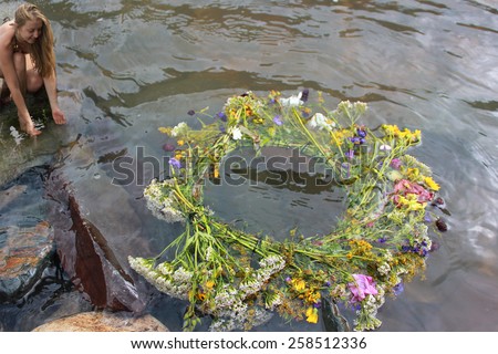Girl releases a wreath from meadow flowers to float on water, hoping, that it will predict good destiny