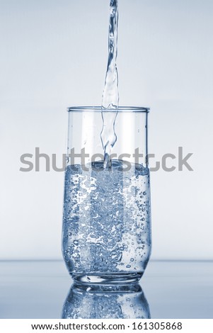 Water Pouring in a Glass over Blue Background