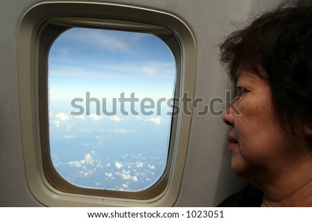 An elderly asian woman looking through the airplane window.