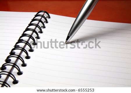 A silver ballpoint pen with its tip resting on a blank page of a notebook.
