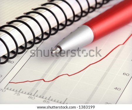 ballpoint pen and notebook on positive earning financial chart