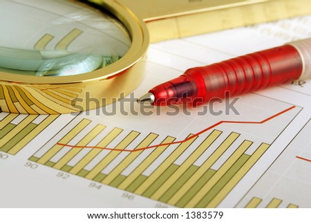 A ball point pen and a magnifying glass on a positive earning chart.