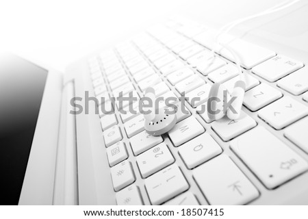 White earphones over a white keyboard suggesting mp3 online buy or download. Small DOF. Focus is on left earphone.