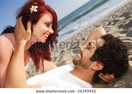 Young couple at the beach laying on sand and posing
